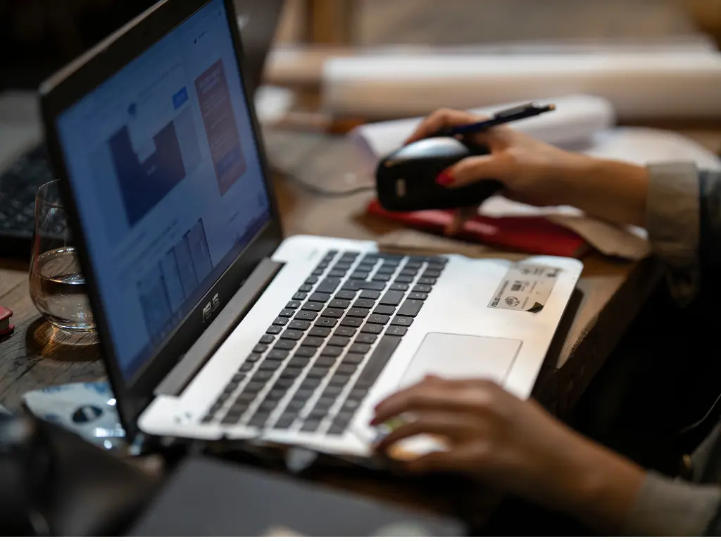 Person working at a laptop, using a mouse, with data charts visible on the screen.