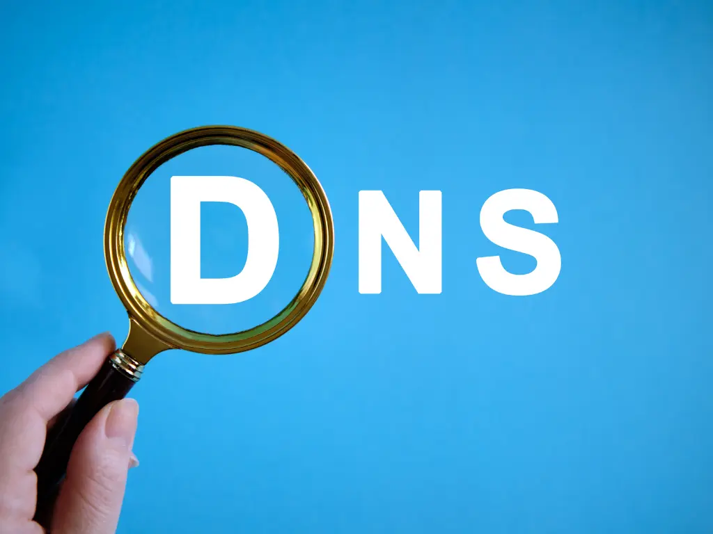 A hand holds a magnifying glass over the letter "D" in the word "DNS" on a blue background.