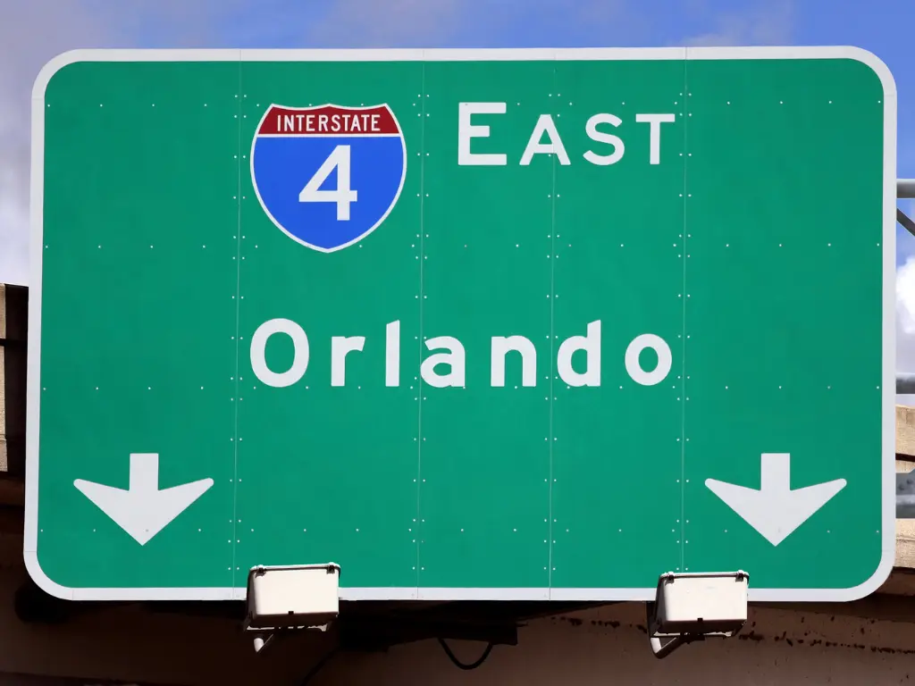 Green overhead highway sign showing Interstate 4 East towards Orlando, with two white arrows pointing downwards.