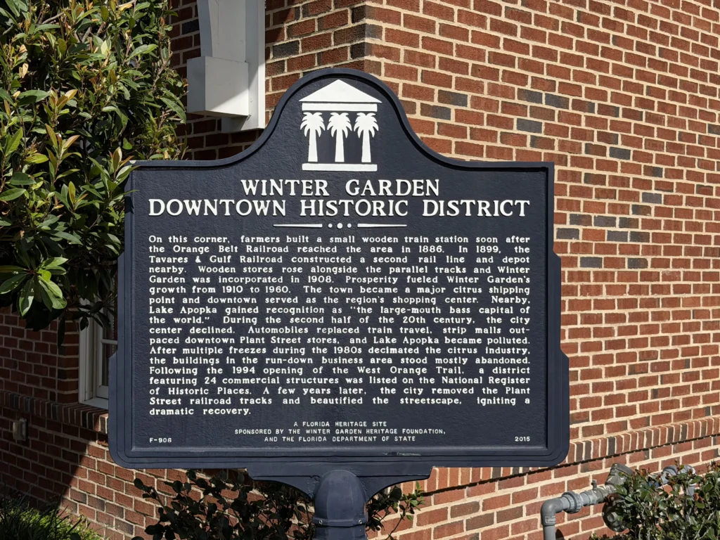 Historic marker sign reading "Winter Garden Downtown Historic District" in front of a brick wall, with detailed text describing the area's historical significance.