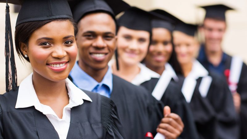 Students in their graduation robes, holding their degrees