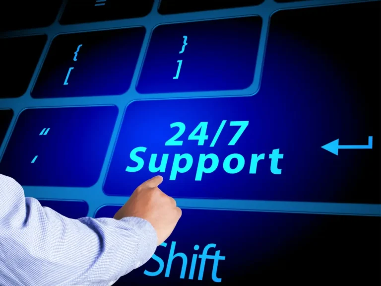 A hand is pressing a large glowing keyboard key labeled “24/7 Support” with surrounding computer keys, highlighting constant support availability.