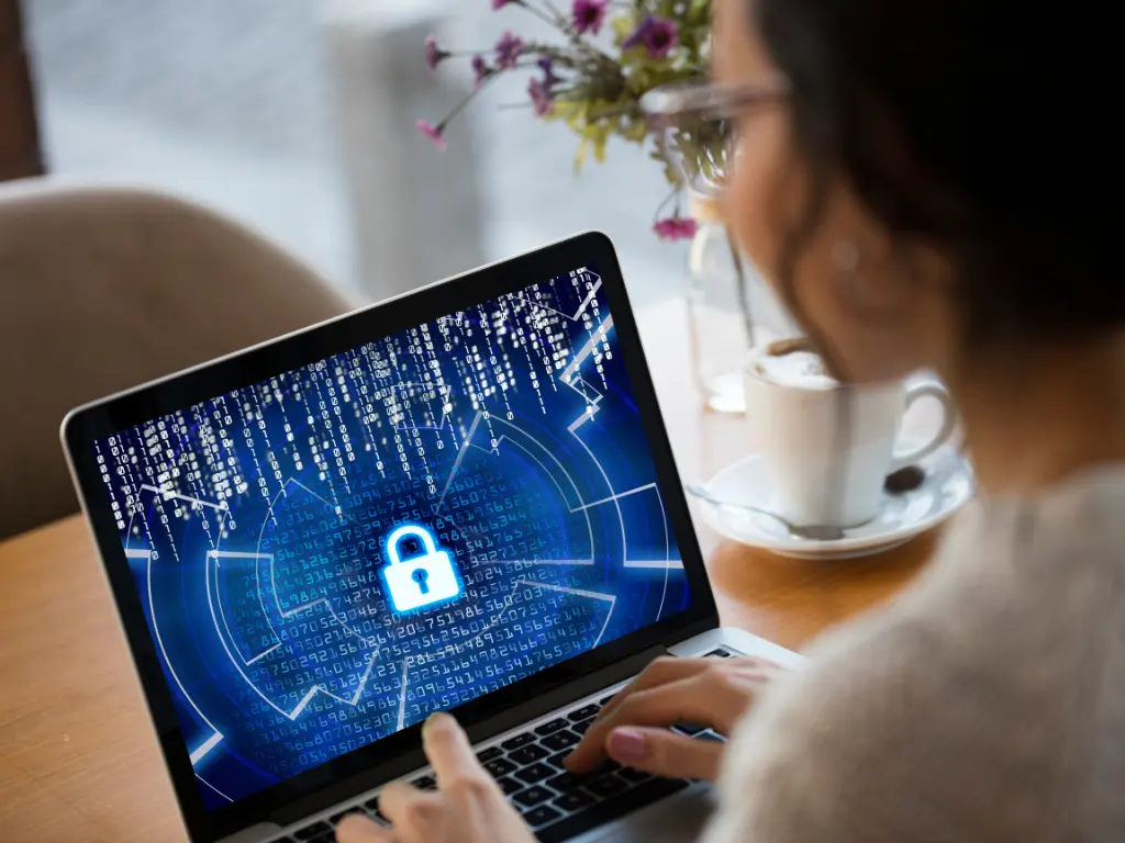 A person using a laptop with a digital lock and cybersecurity graphics displayed on the screen, indicating data protection and security concepts.