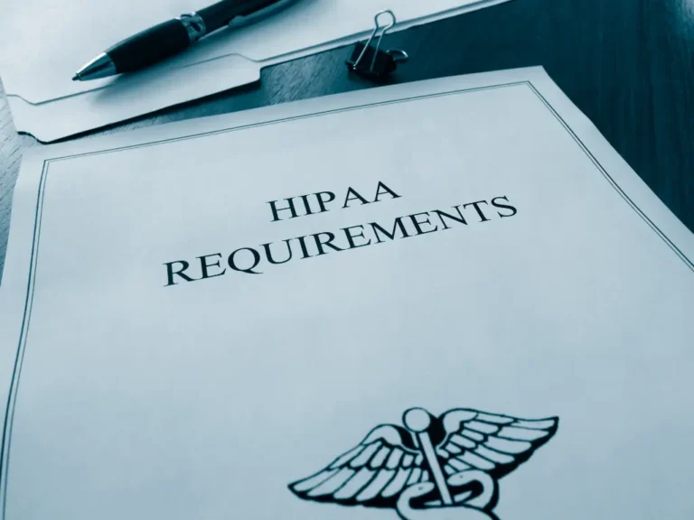 A document titled "HIPAA Requirements" with a medical caduceus symbol, a pen, binder clip, and file folders are on a desk.