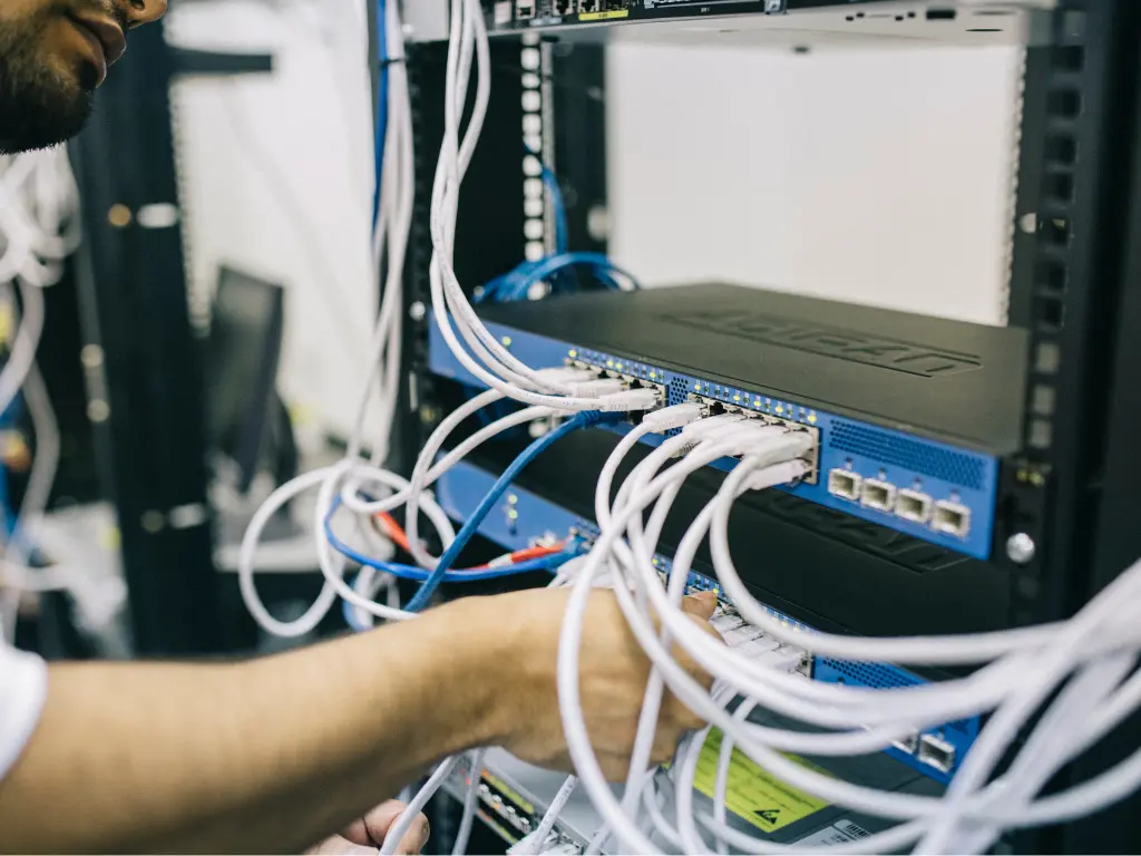 A person connecting and organizing Ethernet cables into a blue network switch in a server rack at a data center.
