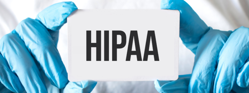 Person wearing blue medical gloves holds a white card with the word "HIPAA" printed in bold black letters.