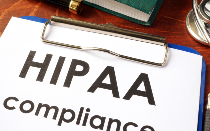 A clipboard with a document titled "HIPAA compliance" and a pen placed on a wooden desk.