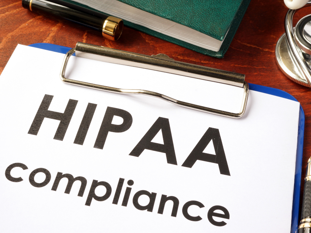 A clipboard with a document titled "HIPAA compliance" and a pen placed on a wooden desk.