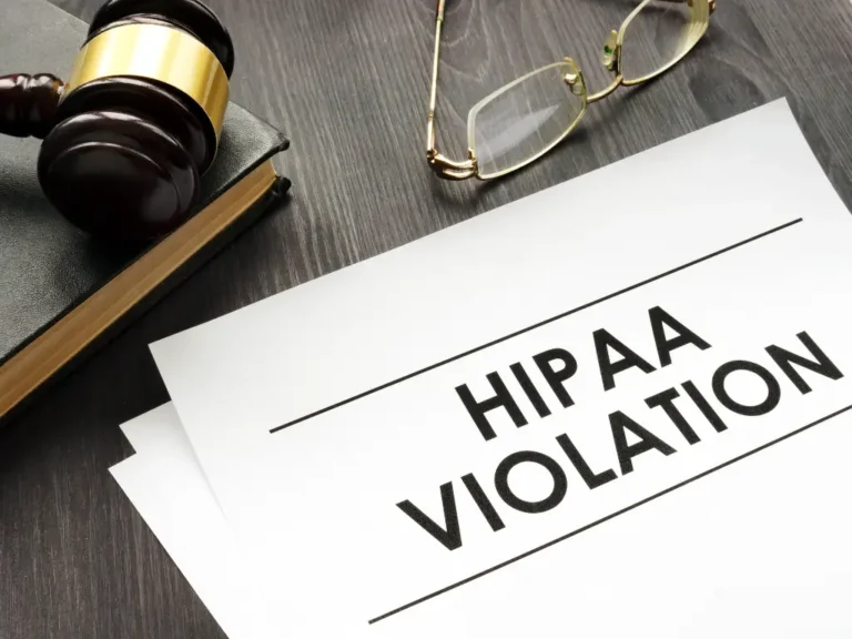 A gavel, eyeglasses, and a document labeled "HIPAA Violation" on a dark wood desk, symbolizing legal or privacy issues.