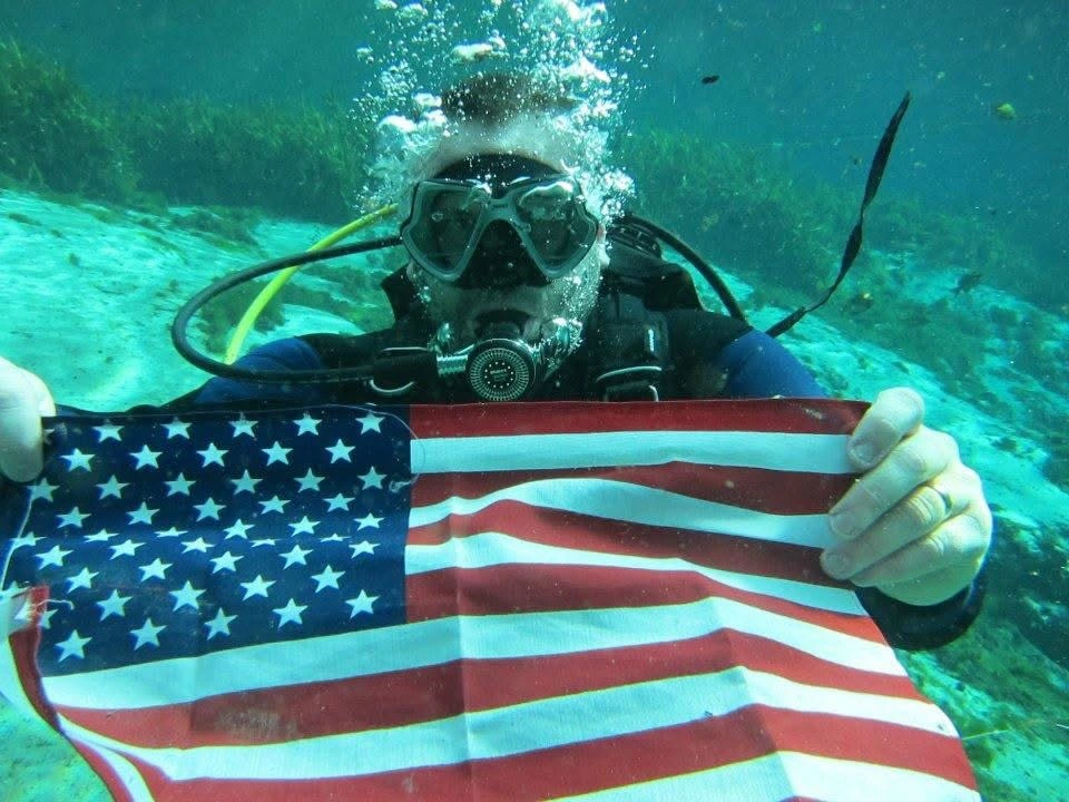 Jason Russell scuba diving in a Florida spring, holding an American flag underwater